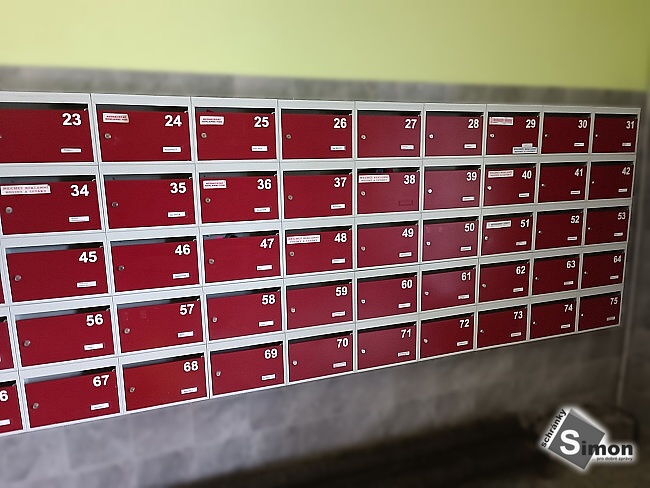 Poštovní schránky tmavě červené s bílým rámem a čísly.
